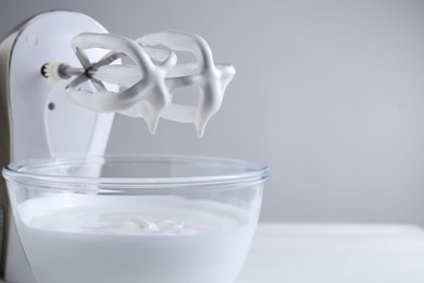 Photo of Hand mixer with whisks and bowl of whipped cream on white table, closeup. Space for text