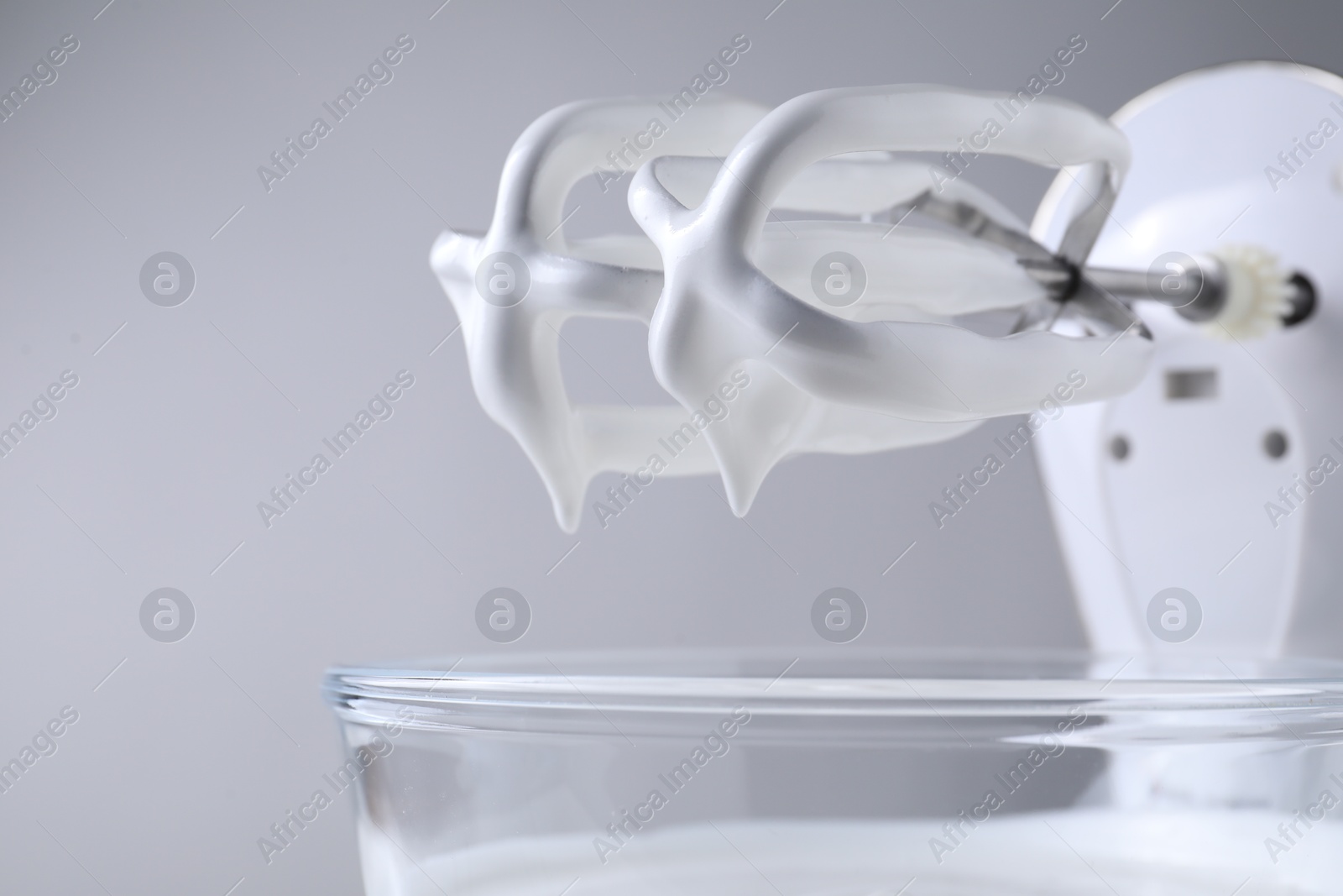 Photo of Hand mixer with whisks and bowl of whipped cream on light grey background, closeup