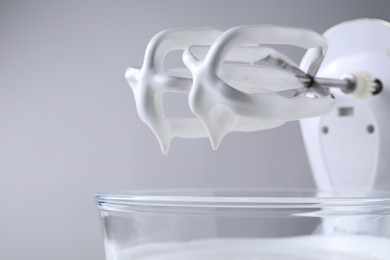 Photo of Hand mixer with whisks and bowl of whipped cream on light grey background, closeup