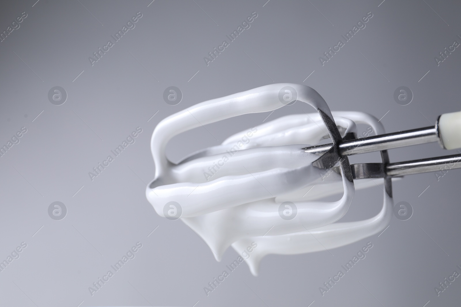 Photo of Hand mixer with whisks and whipped cream on grey background, closeup