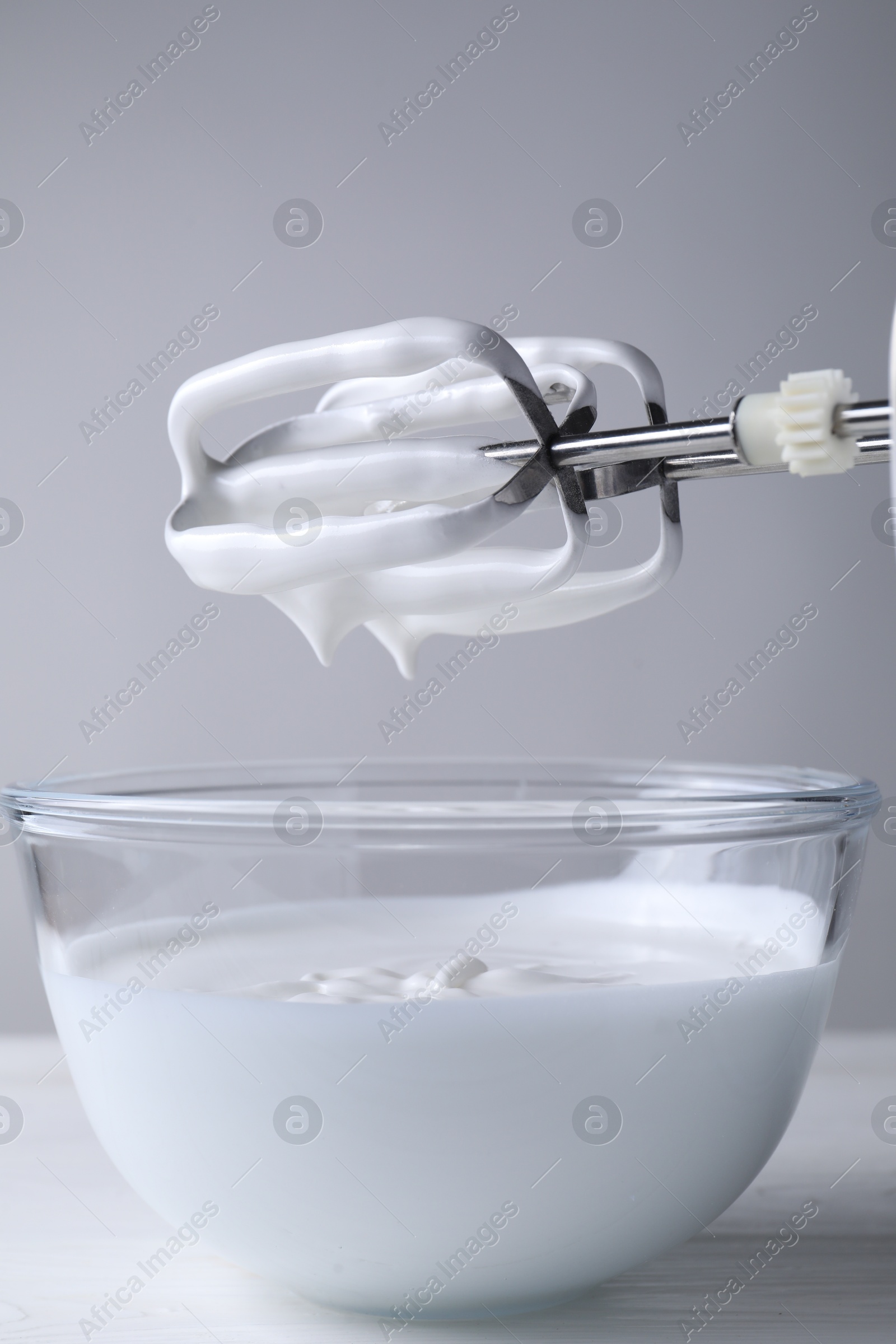 Photo of Hand mixer with whisks and bowl of whipped cream on white wooden table, closeup