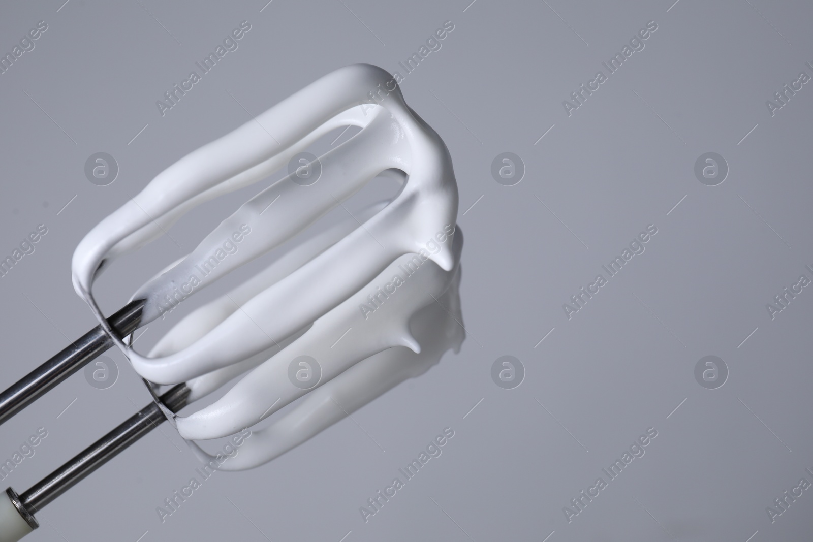 Photo of Whisks with whipped cream on light grey background, closeup. Space for text