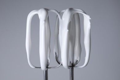 Photo of Whisks with whipped cream on light grey background, closeup