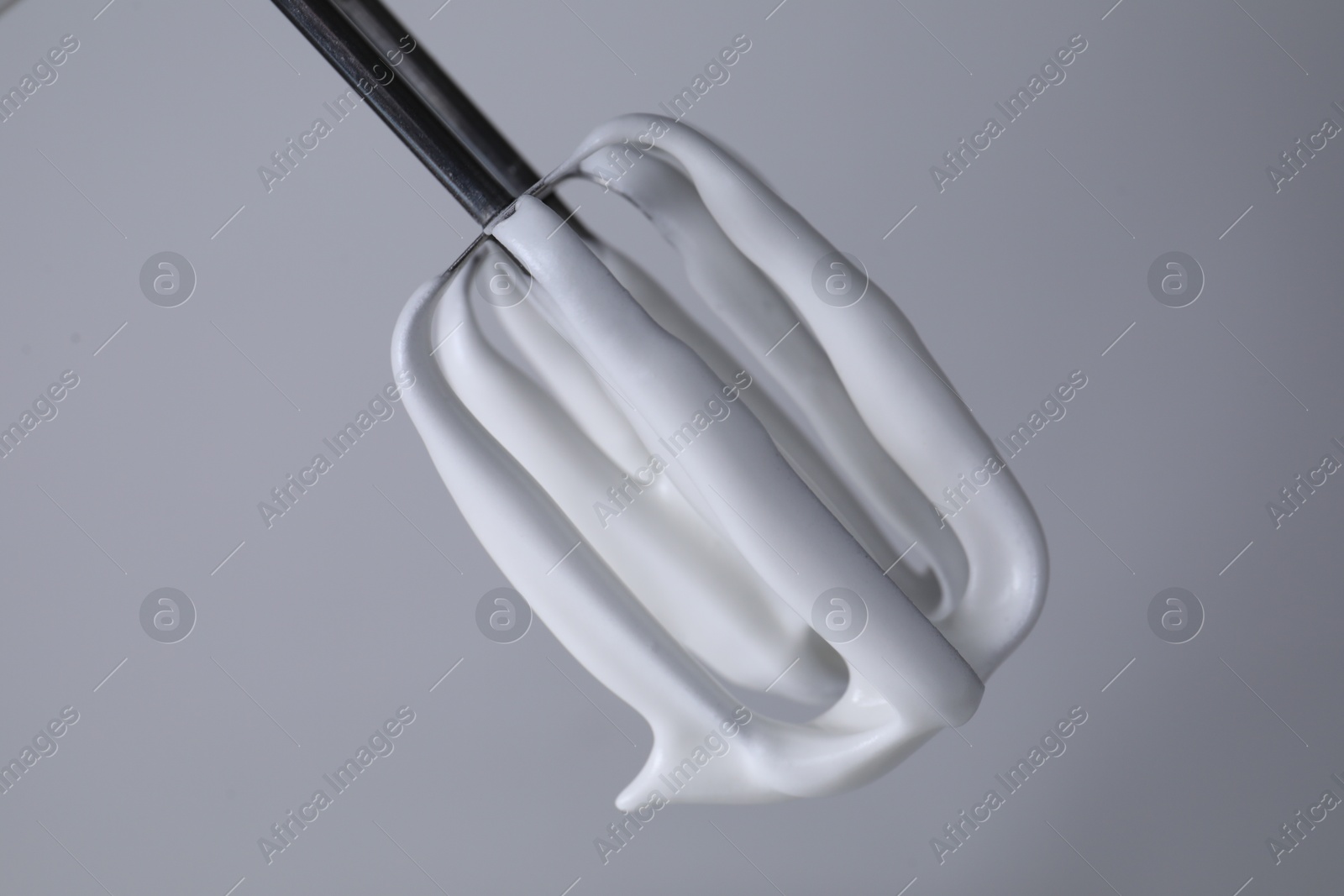 Photo of Whisk with whipped cream on light grey background, closeup