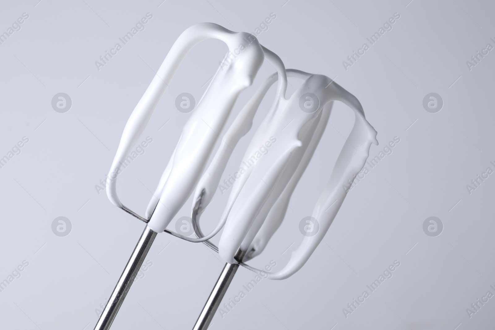 Photo of Whisks with whipped cream on white background, closeup