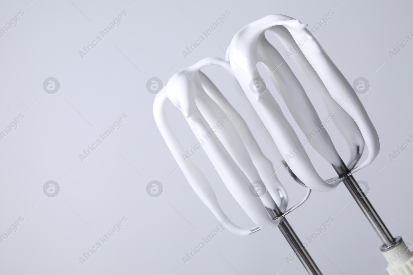 Photo of Whisks with whipped cream on white background, closeup. Space for text