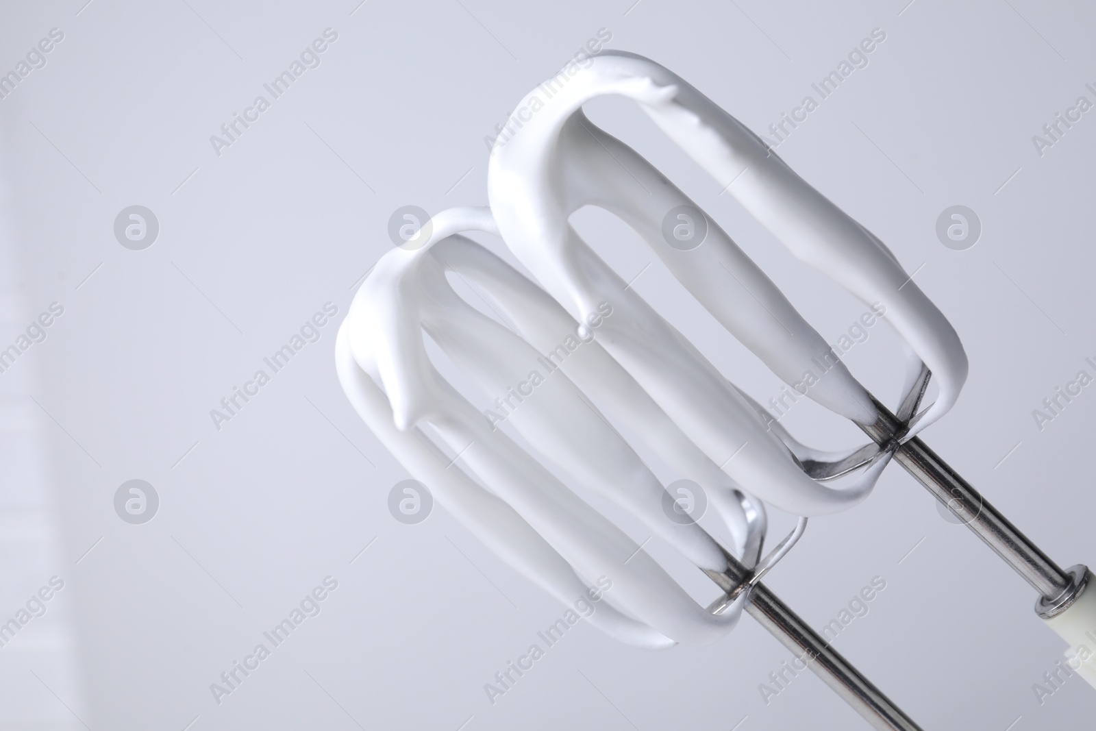 Photo of Whisks with whipped cream on white background, closeup