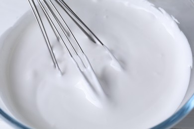 Photo of Whisk and whipped cream in bowl, closeup