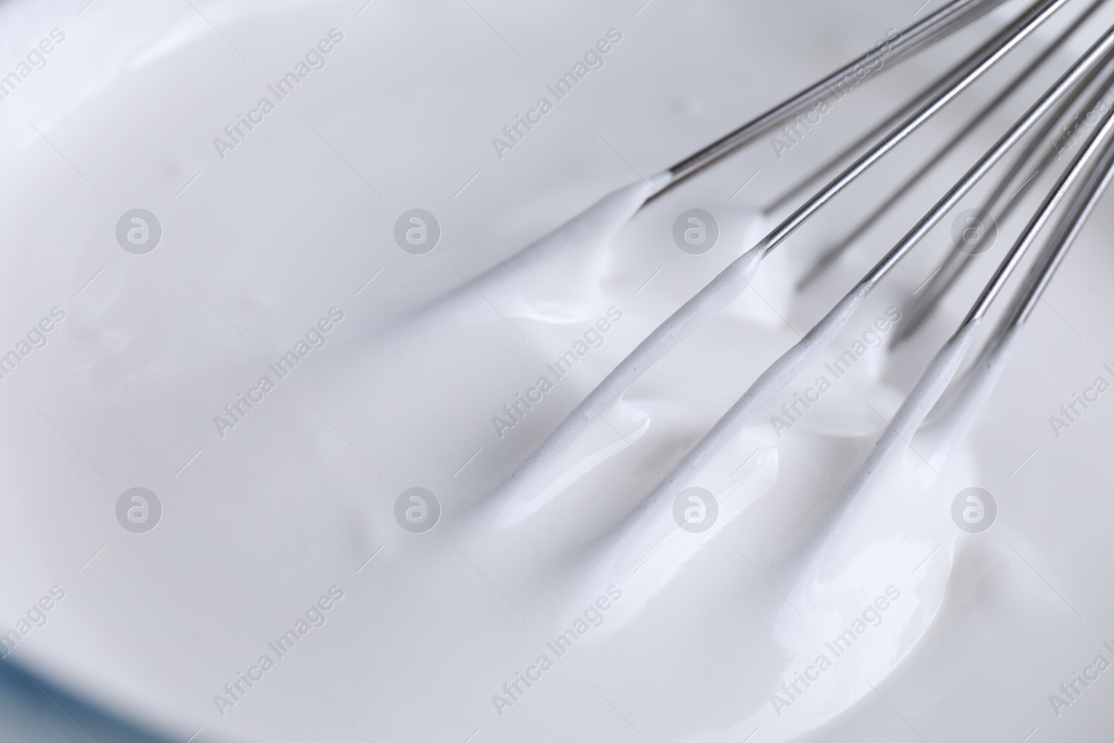 Photo of Whisk and whipped cream in bowl, closeup