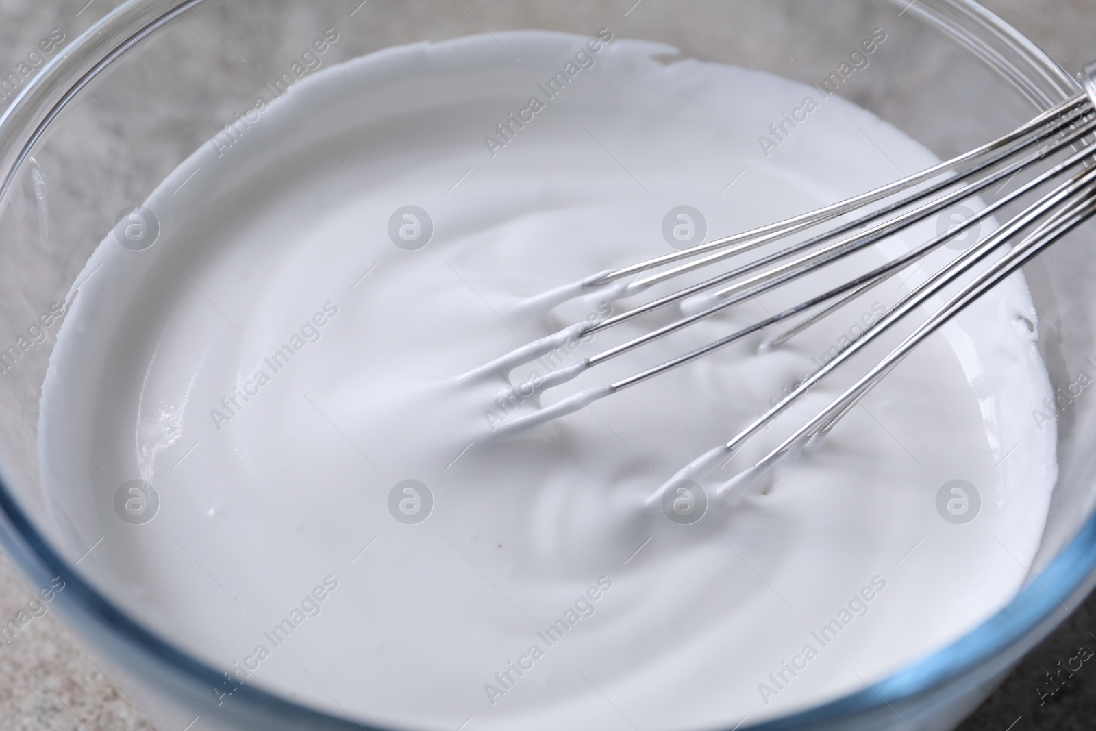 Photo of Whisk and bowl with whipped cream on grey table, closeup