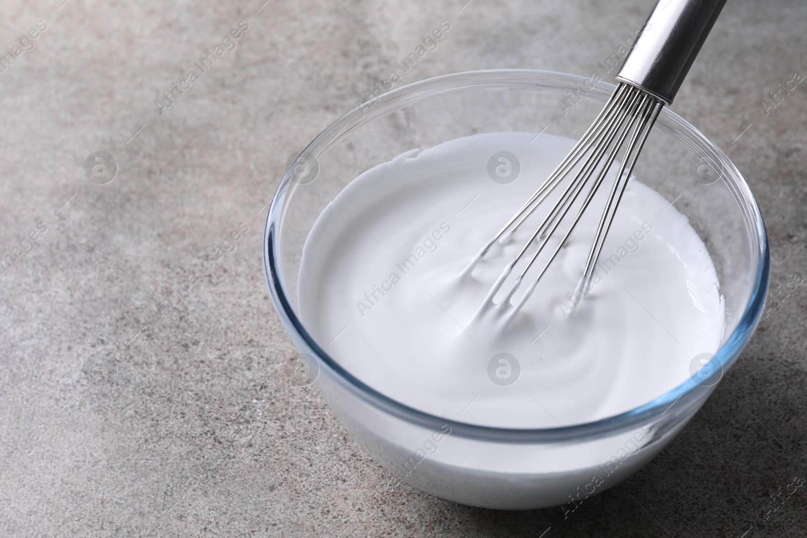 Photo of Whisk and bowl with whipped cream on grey table, space for text