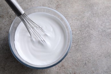 Photo of Whisk and bowl with whipped cream on grey table, top view. Space for text