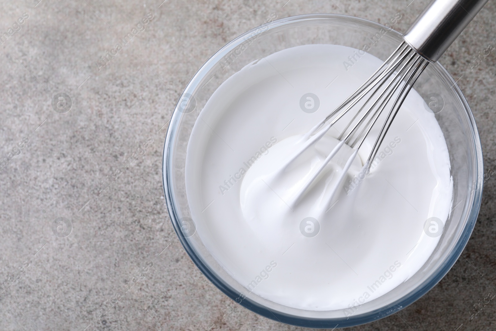 Photo of Whisk and bowl with whipped cream on grey table, top view. Space for text