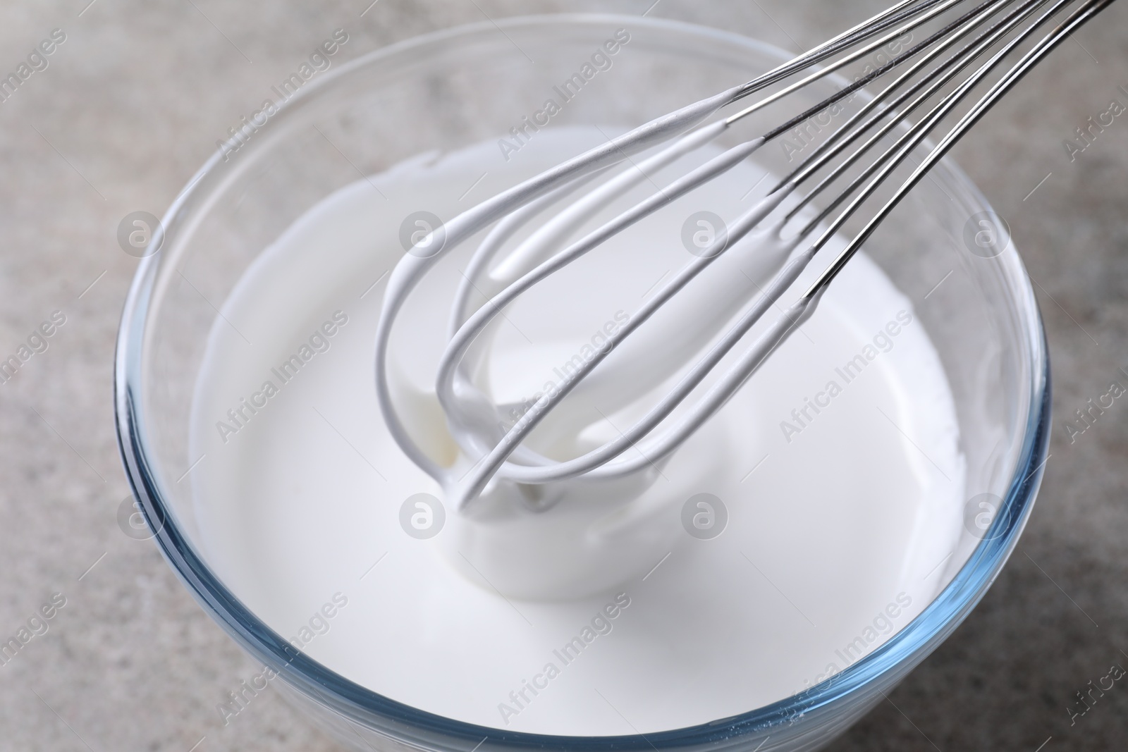 Photo of Whisking whipped cream in bowl on grey table, closeup