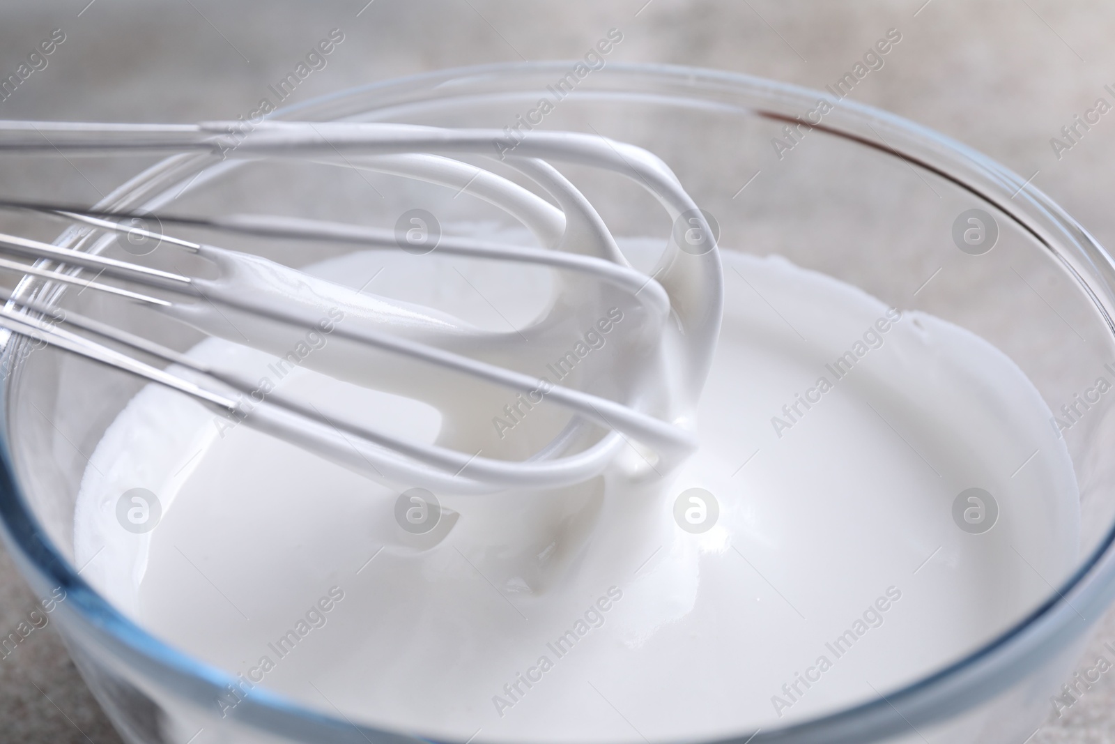 Photo of Whisking whipped cream in bowl on grey table, closeup