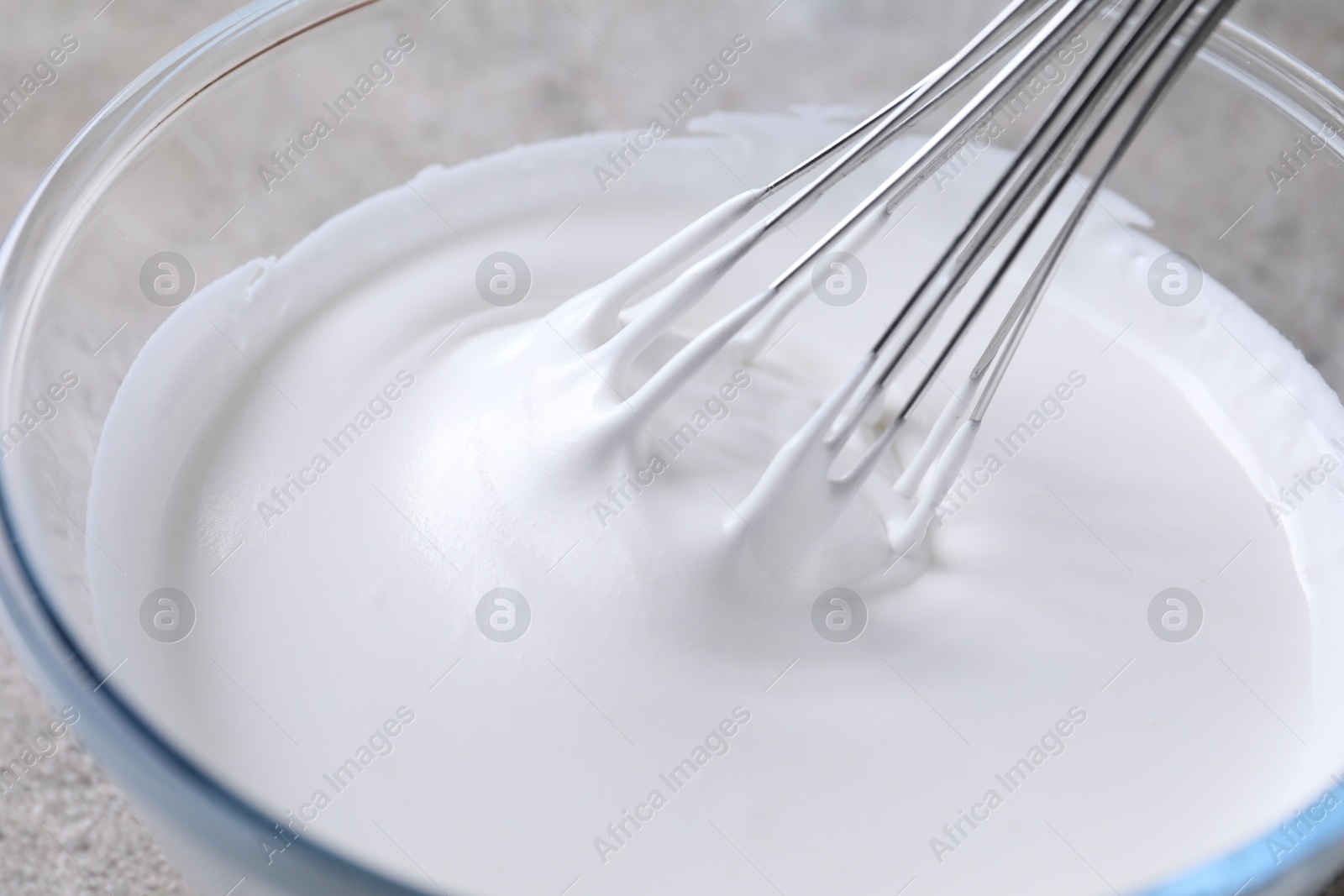 Photo of Whisking whipped cream in bowl on grey table, closeup