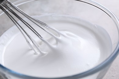 Photo of Whisking whipped cream in bowl on grey table, closeup