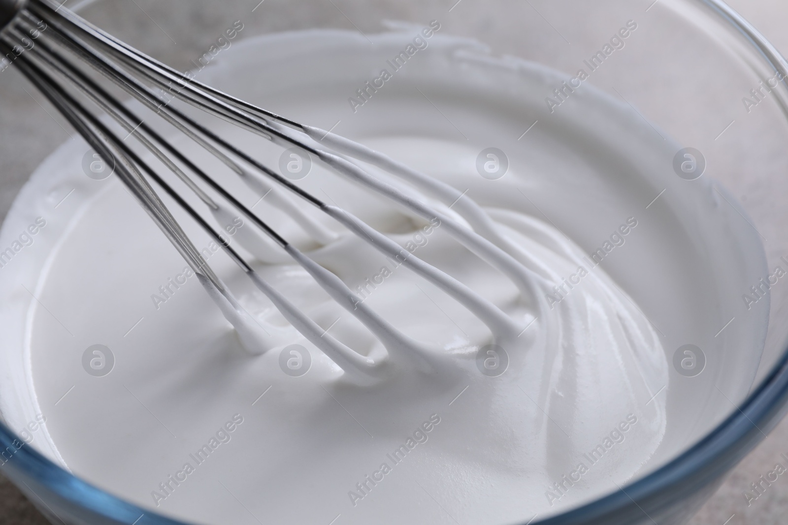 Photo of Whisking whipped cream in bowl on grey table, closeup