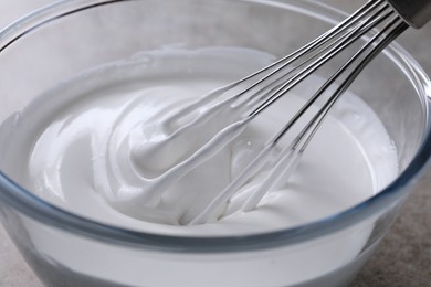 Photo of Whisking whipped cream in bowl on grey table, closeup