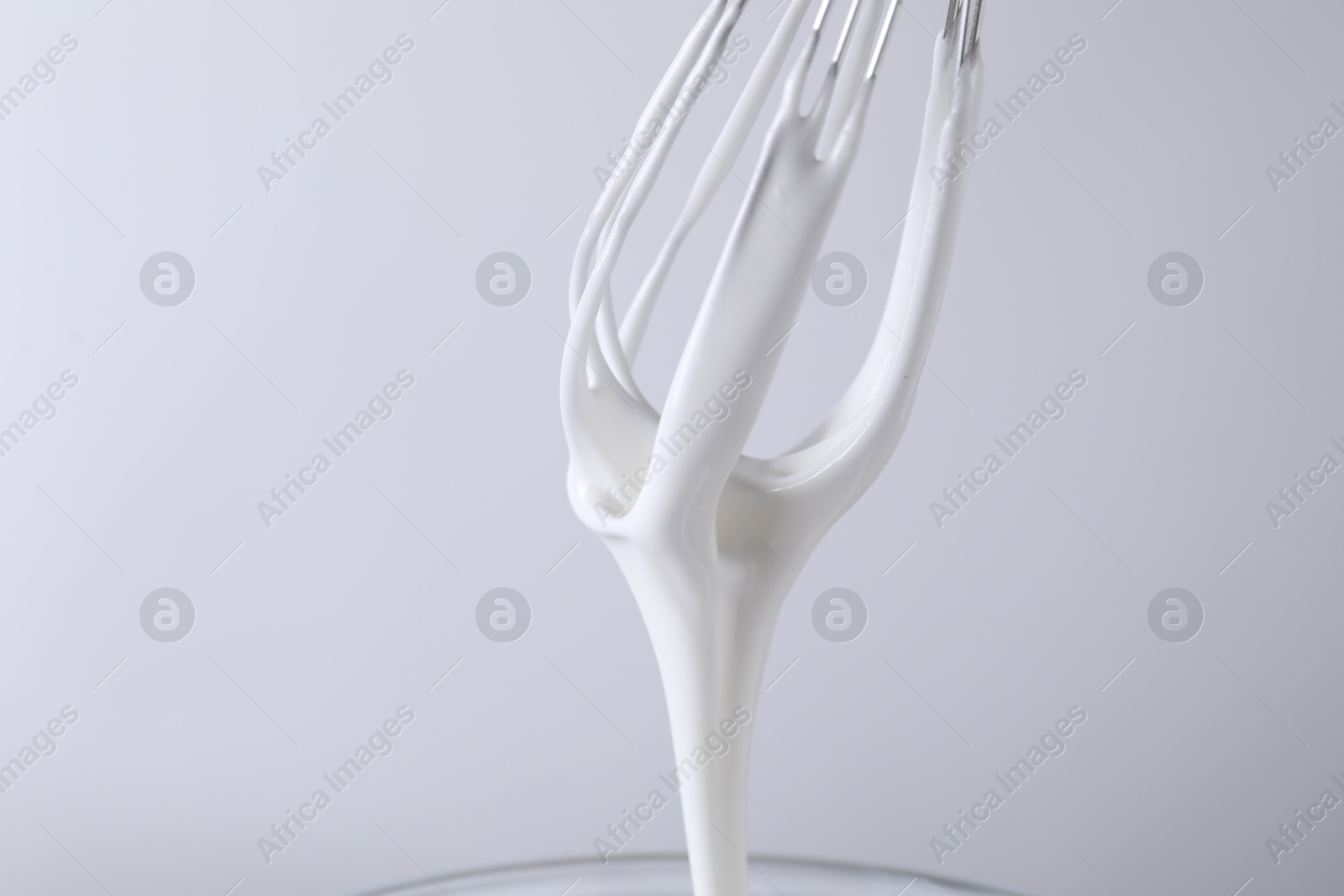 Photo of Whisk with whipped cream on white background, closeup