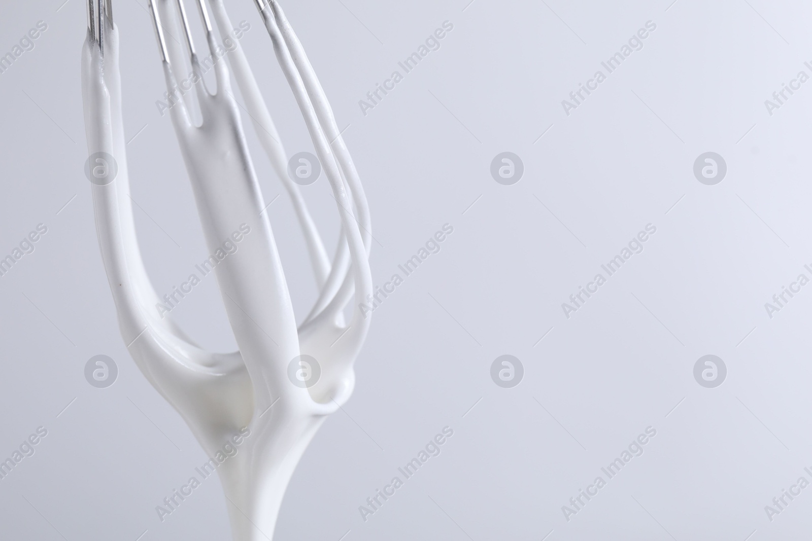 Photo of Whisk with whipped cream on white background, closeup. Space for text