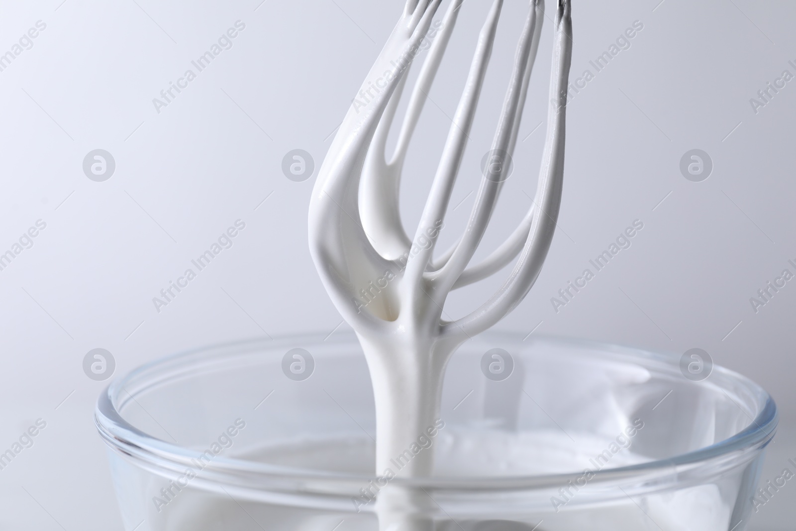 Photo of Whisk and bowl with whipped cream on white background, closeup