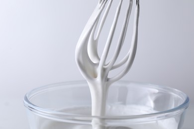 Photo of Whisk and bowl with whipped cream on white background, closeup