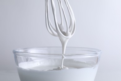 Photo of Whisk and bowl with whipped cream on white background, closeup