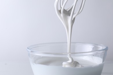 Photo of Whisk and bowl with whipped cream on white background, closeup