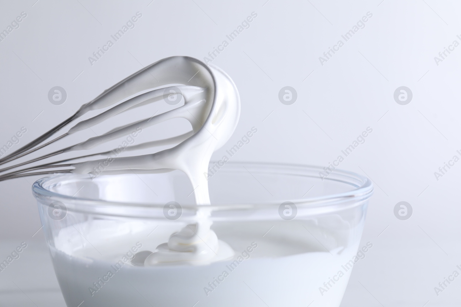 Photo of Whisk and bowl with whipped cream on white background, closeup