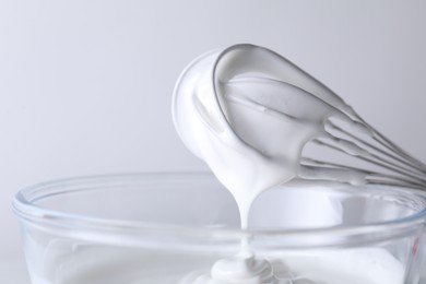 Photo of Whisk and bowl with whipped cream on white background, closeup