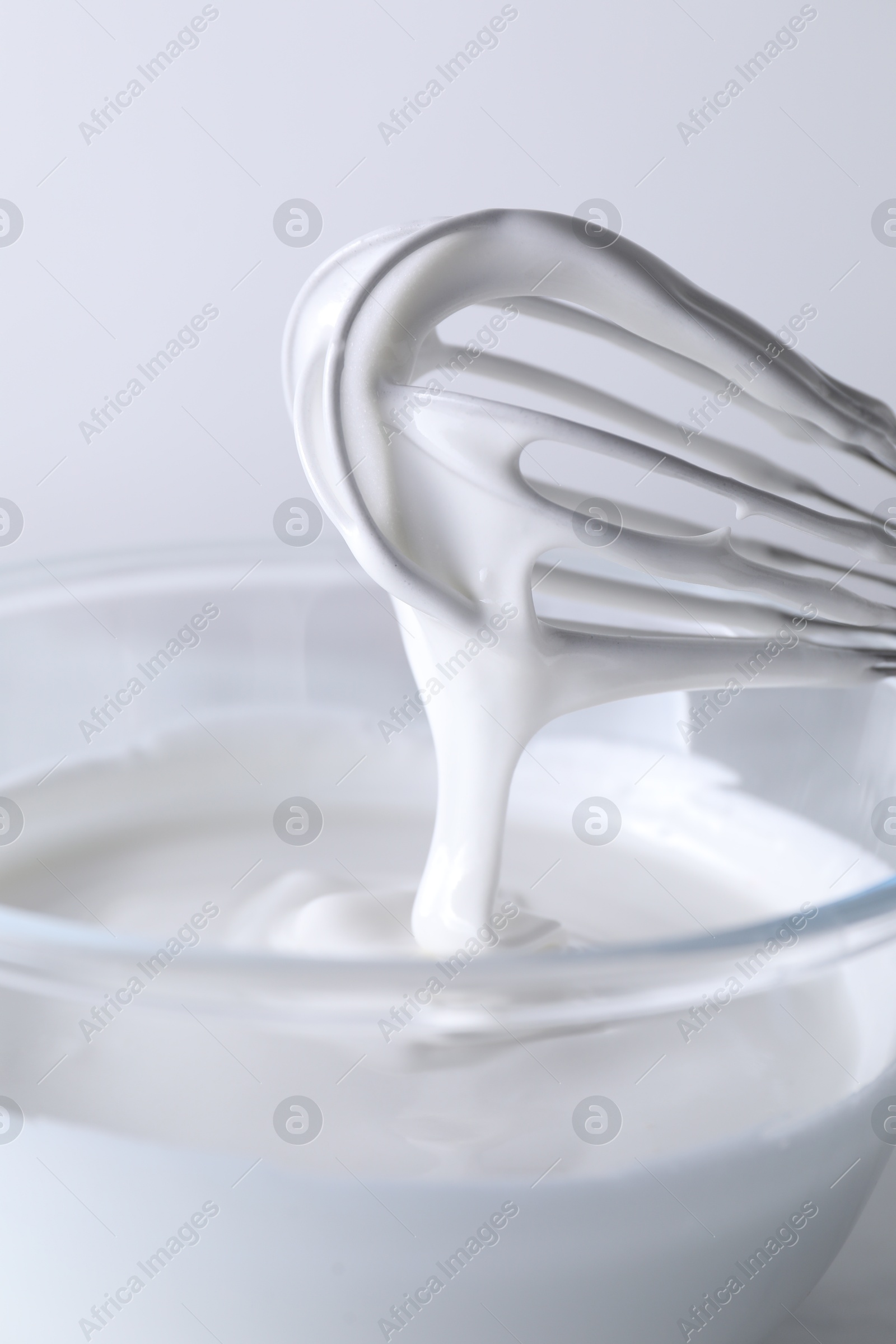 Photo of Whisk and bowl with whipped cream on white background, closeup