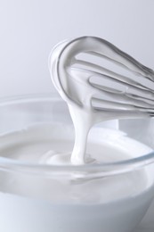 Photo of Whisk and bowl with whipped cream on white background, closeup