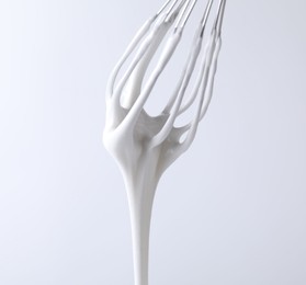 Photo of Whisk with whipped cream on white background, closeup