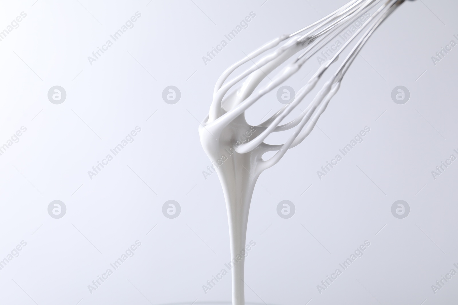 Photo of Whisk with whipped cream on white background, closeup. Space for text