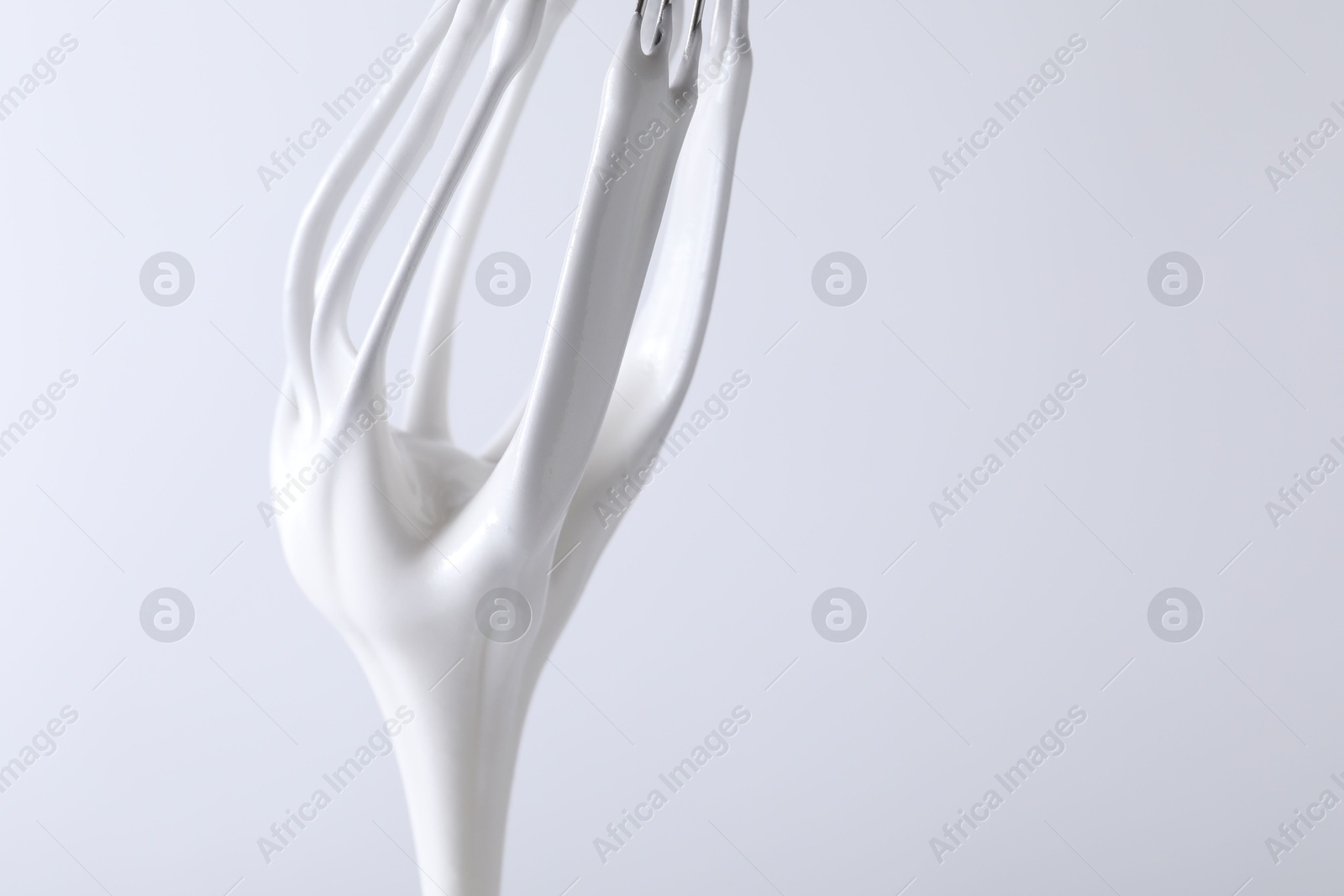 Photo of Whisk with whipped cream on white background, closeup. Space for text