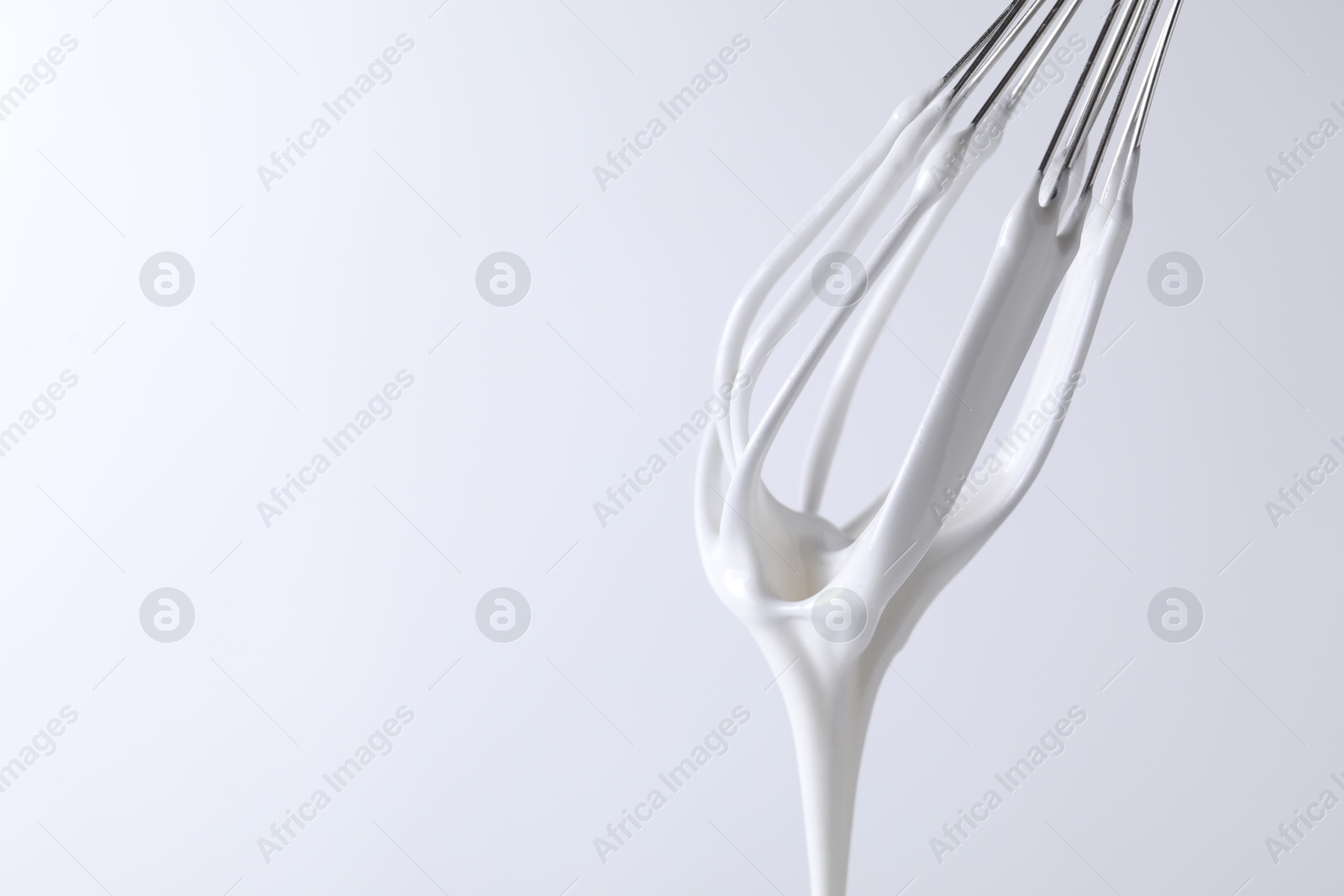 Photo of Whisk with whipped cream on white background, closeup. Space for text