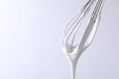 Photo of Whisk with whipped cream on white background, closeup. Space for text