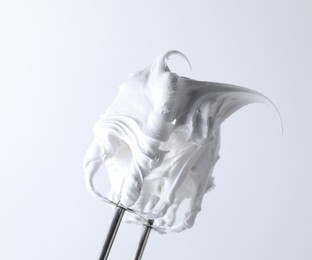 Photo of Whisk with whipped cream on white background, closeup