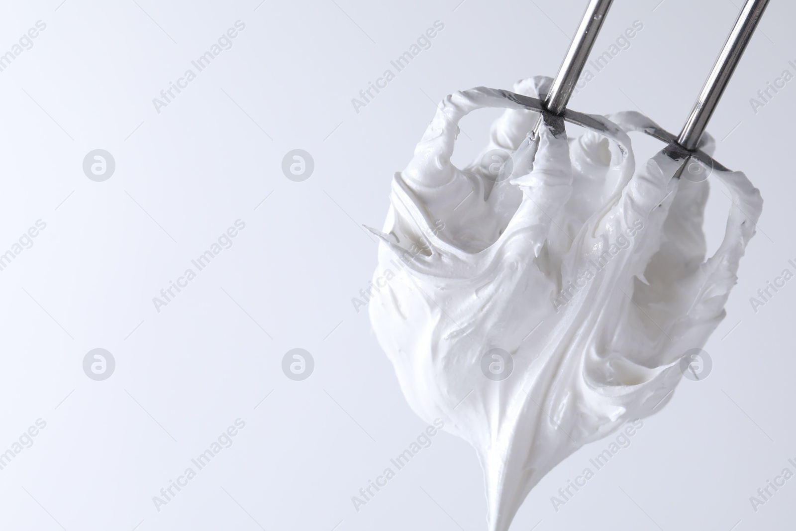 Photo of Whisks with whipped cream on white background, closeup. Space for text