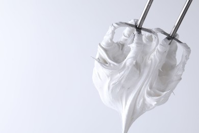 Photo of Whisks with whipped cream on white background, closeup. Space for text