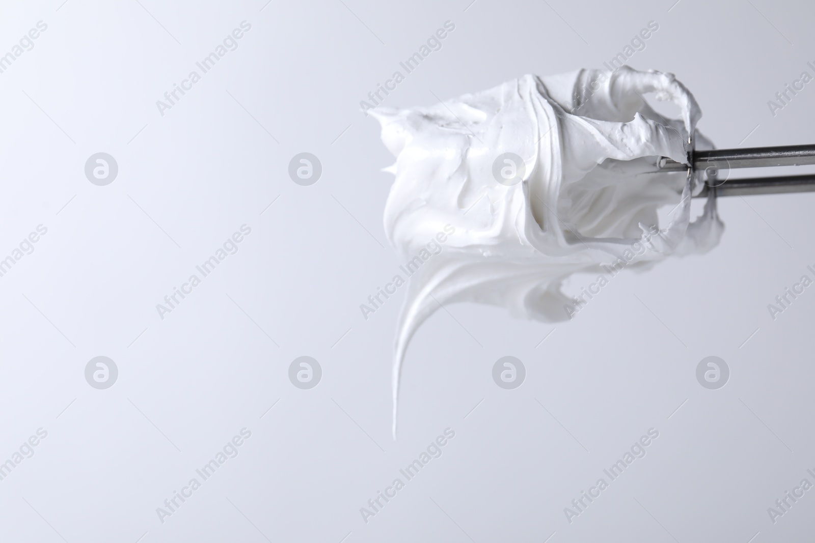 Photo of Whisks with whipped cream on white background, closeup. Space for text