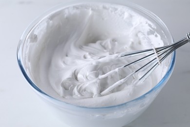 Photo of Bowl with whisk and whipped cream on white table, closeup