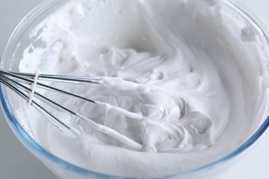 Photo of Bowl with whisk and whipped cream on white table, closeup