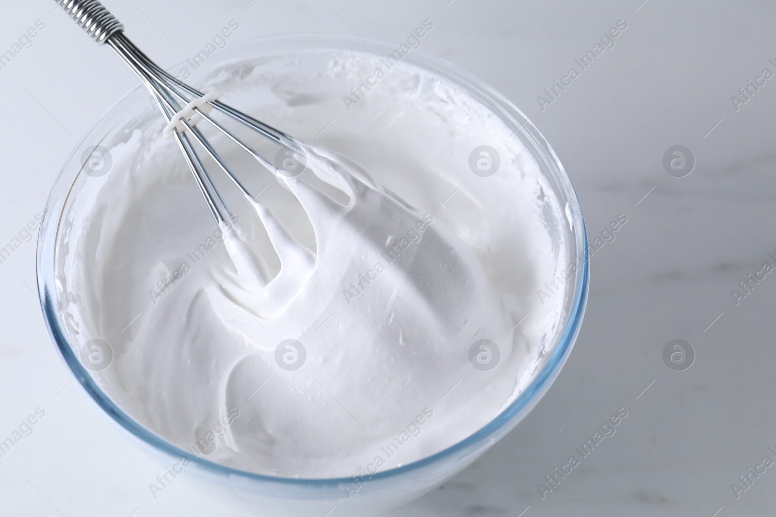 Photo of Bowl with whisk and whipped cream on white marble table, closeup