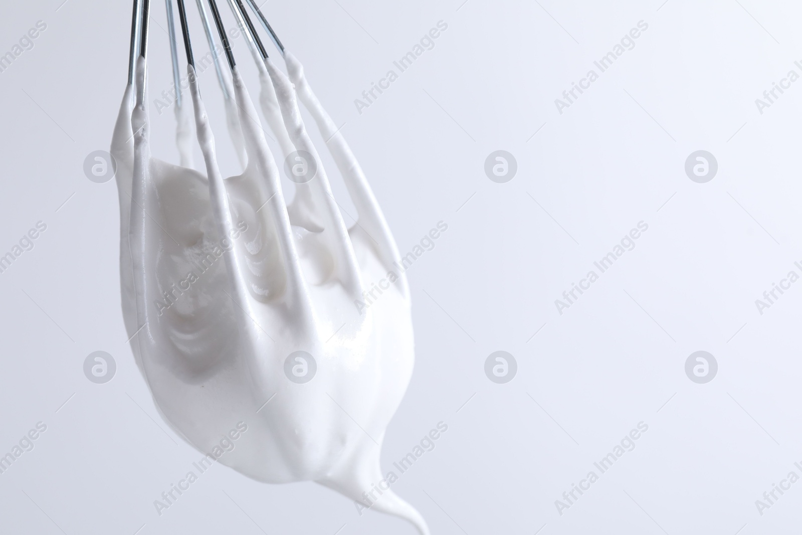 Photo of Whisk with whipped cream on white background, closeup. Space for text