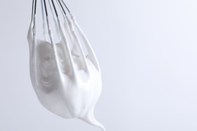 Photo of Whisk with whipped cream on white background, closeup. Space for text