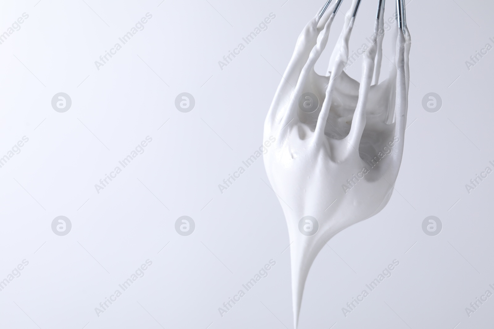 Photo of Whisk with whipped cream on white background, closeup. Space for text