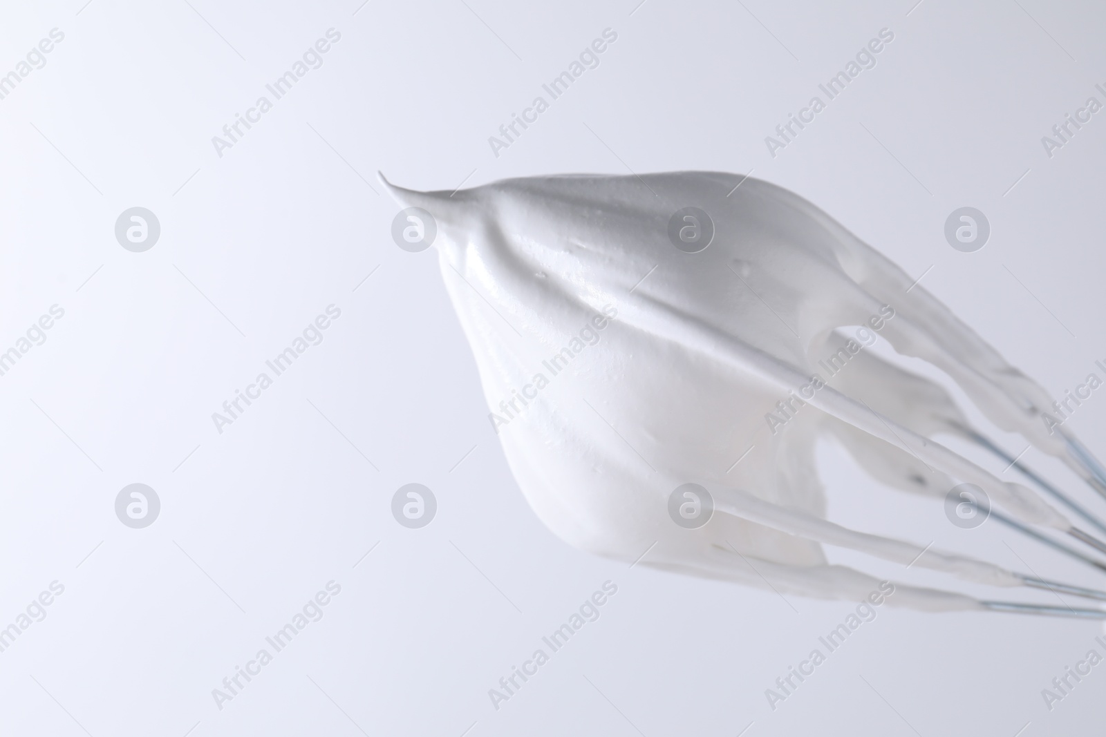 Photo of Whisk with whipped cream on white background, closeup. Space for text