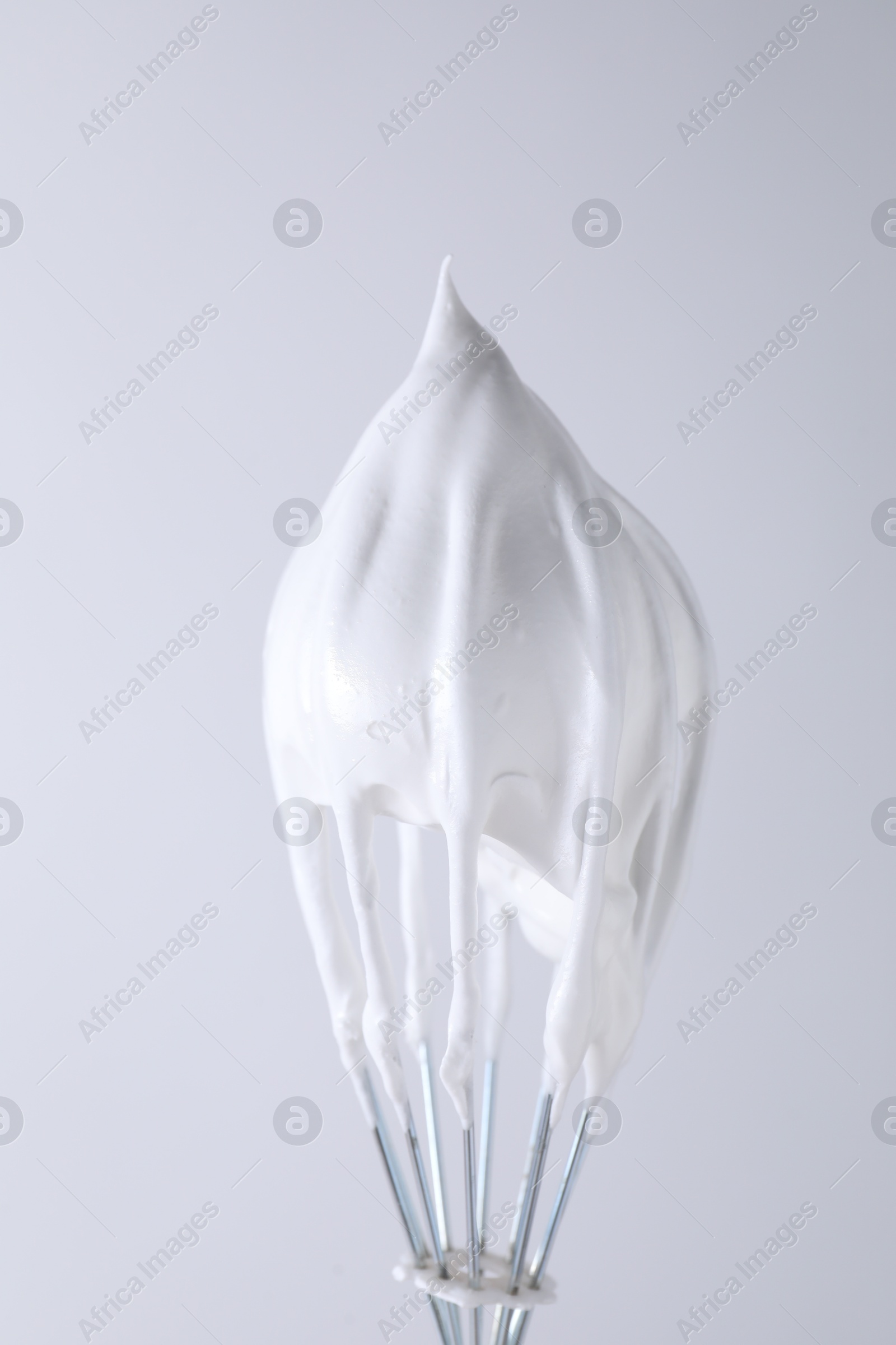 Photo of Whisk with whipped cream on white background, closeup